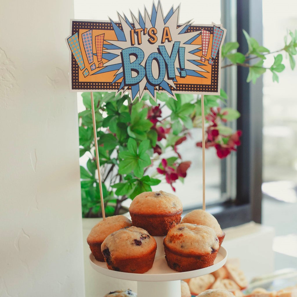 Decorative sign with 'It's a Boy!' text above muffins on a stand.